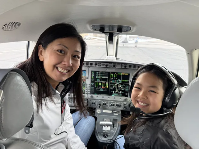 A woman and a young girl wearing headsets smile from the cockpit of a small aircraft