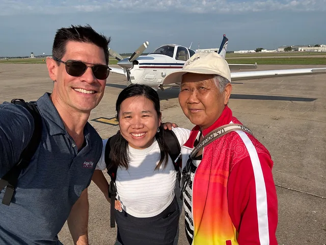 Three people stand together on the ramp in front of a single-engine aircraft on a clear day