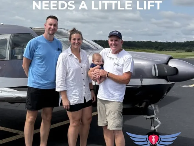 A family holding a baby stands with a volunteer pilot beside a small aircraft