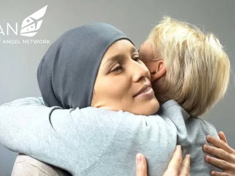 Two women embrace cheek to cheek; one wears a soft head covering during cancer treatment