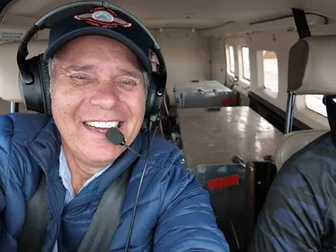 A smiling volunteer pilot wearing a headset flies a small aircraft, with a second pilot in the right seat