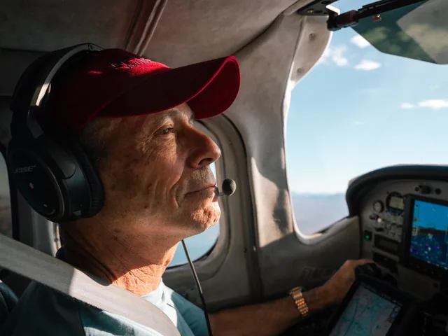 A LightHawk volunteer pilot in a red cap and headset flies a small aircraft with terrain visible through the windscreen