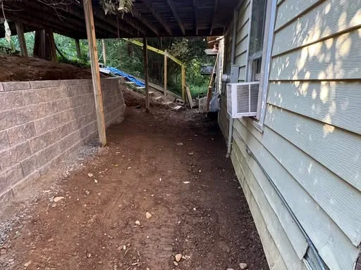 A newly built block retaining wall runs along a dirt path beside a house